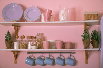 Kitchenware on white shelves in the kitchen. Cups, plates and glass bottles.