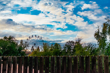 Cloudy evening sky over a residential area, over a wooden fence. Overcast gray clouds over a yellow sunset, through trees and blue dark saturated sky