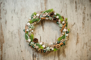 Beautiful Christmas wreath decorated with green spruce branches, pine cones, white berries and cinnamon sticks.