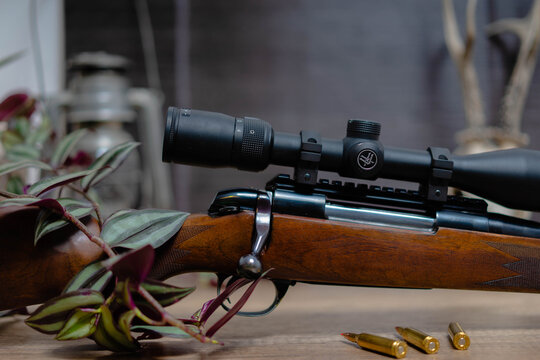 Side view of beautiful rifle with wood stock. Caliber 22 long rifle. Ammunition on table. Bolt action rifle with scope mount.