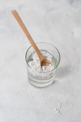Close-up collagen powder in a spoon with a glass of water , on concrete background.