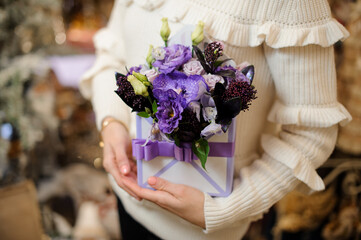 Creative flower arrangement in square box decorated with ribbon in female hands.