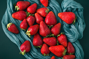 Red strawberries on a gauze cloth. Fresh ripe berries on a dark green fabric background