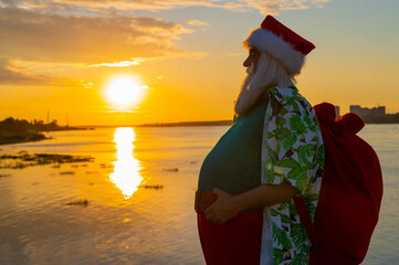 Santa claus in shorts and a shirt walks along the beach at sunset. Christmas in a hot country