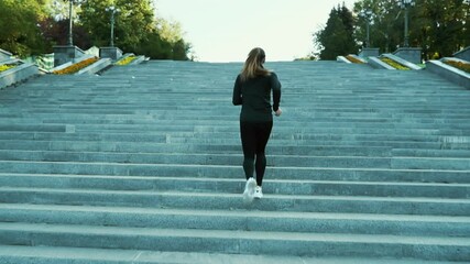 Young woman with ponytail wearing black sportswear running up long staircase in city in slow motion. Following shot of female athlete doing cardio training in the morning. Concept of fitness - Powered by Adobe
