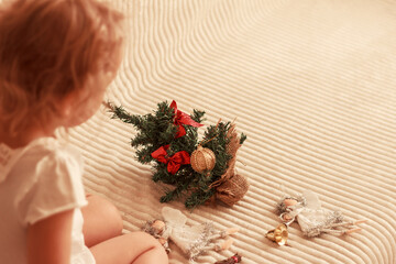 Little Christmas tree on light background, two angle decorations and a child sitting near the tree. Merry christmas and happy new year concept. Empty space for text