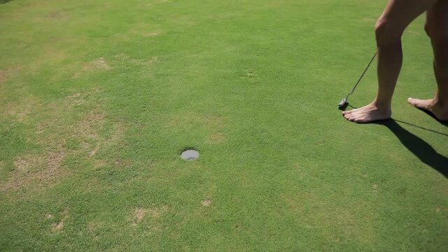 A man without shoes plays golf on a hot summer day.