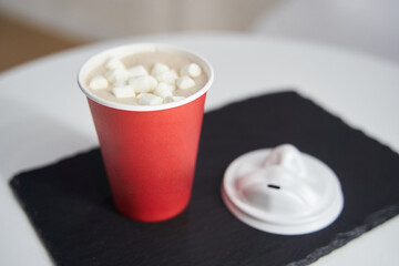 Red paper cup of coffee with marshmallows on a black tray.