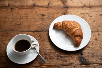 breakfast on the wooden table with a croissant and a cup of coffee.