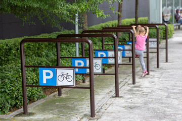 Obraz premium Empty place for a parking of bicycles. Little girl in a pink t-shirt near the parking lot for a bicycle. Rear view - Image.