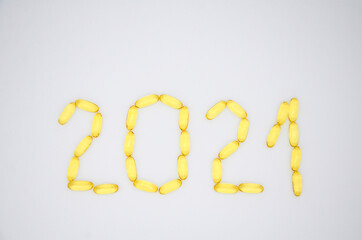 Number 2021 of yellow transparent omega 3 capsules and stars on a white background. Creative concept of a healthy lifestyle and proper nutrition. Christmas medical flat lay.