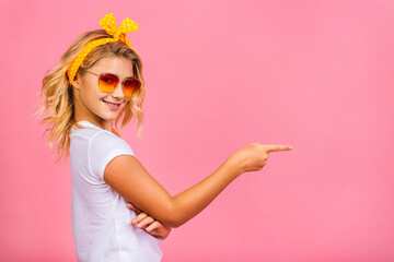 Smiling little kid girl 12-13 years old in casual isolated on pink background children studio portrait. Childhood lifestyle concept. Mock up copy space. Pointing finger.