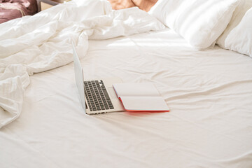 the laptop is on the bed, next to it is an open notebook