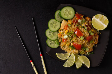Khao Pad, fried rice with vegetables, meat and eggs, with fresh cucumbers, tomatoes, with chopsticks.