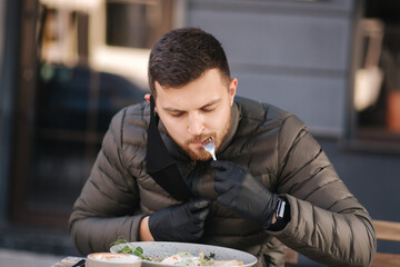 Man in black gloves hold cutlery. Quarantine Cafe concept. Food outdoors in protective gloves....