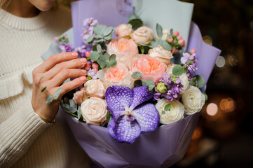 close-up of cute bouquet of fresh flowers wrapped in purple paper in female hands