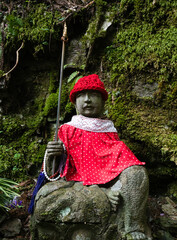 Buddhist Jizo statue in red garments on a mountain path leading to Iwayaji, temple number 45 of...