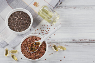 Brown flax seed or linseed and chia in small bowl and gelatin capsules with omega oil on a white...
