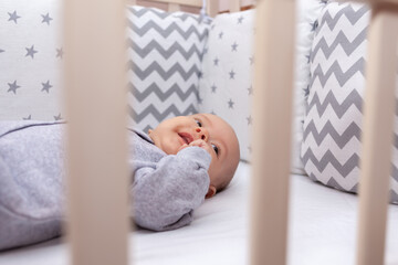 Newborn baby girl in a crib in gray pajamas. Selective focus