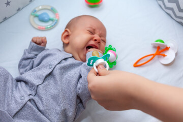 mom tries to give a pacifier to a crying baby. Selective focus