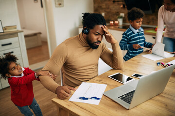 African American father working on laptop while his daughter wants to play with him at home.