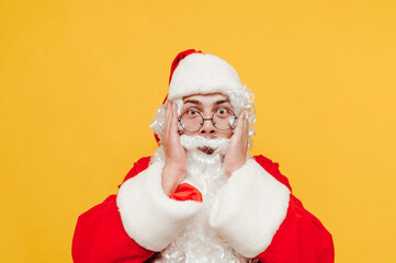 Emotional Santa Claus is touching his head with his hands, looking at the camera, feeling shocked, worried and stressed before Christmas holidays.