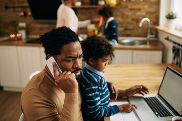 Black stay at home father talking on the phone while working at home.