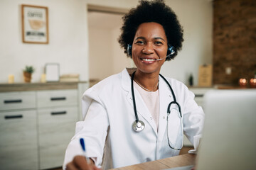 Happy black female doctor working at her office and looking at camera. - obrazy, fototapety, plakaty