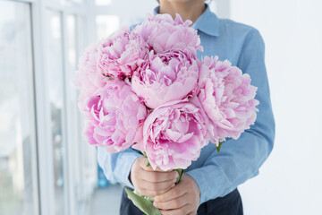 close up image of boy in blue shirt hold big gentle bouquet of pink peony. Congratulations with birthday, mother's day, anniversary, valentines day. Holiday concept