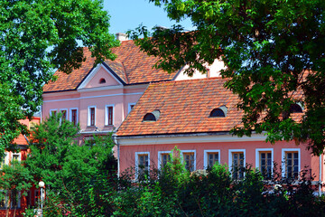 Fototapeta na wymiar Facades of historic houses in Trinity Suburb or Trinity Hill (Trajeckaje pradmiescie) - the oldest surviving district of Minsk. Green trees on a foreground. Summertime in Republic of Belarus.