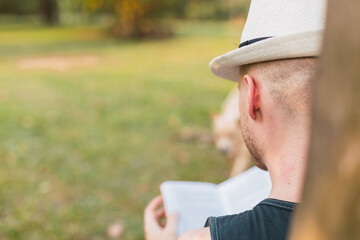 Back view of a young man reading a book in the garden - Young relaxed man reading book in nature, back in the tree.