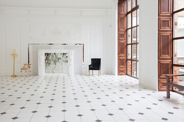 Fototapeta premium Huge luxury white hall with unique interior. Black and white tiles on the floor, white and black stucco on the walls, high fireplace with mirror mosaic, three-meter crystal chandelier and grand piano