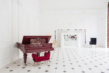 Huge luxury white hall with unique interior. Black and white tiles on the floor, white and black stucco on the walls, high fireplace with mirror mosaic, three-meter crystal chandelier and grand piano
