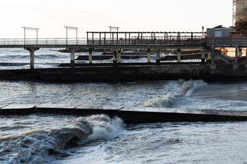 Pier on the coast on the background of the raging sea in sunny weather.
