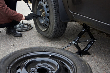 A woman removes the wheel with a key near her car with a flat tire.