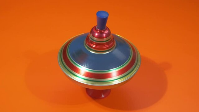 Multicolored metal spinning top or whirligig top is traditional toy for preschool childs. Rotates in circle on orange surface.