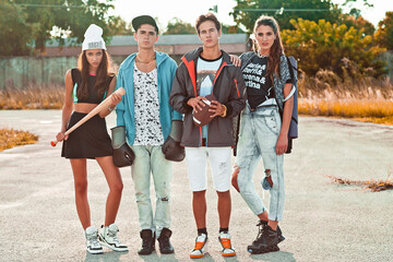 Portrait of an interracial group of 4 young adults standing together on and old parking lot in front of an old graffiti sprayed store front during a warm summer day wearing sportive urban outfits.