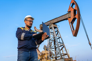 Engineer with a laptop against the background of oil rockers.