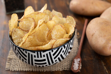 Bowl full of potato chips with raw potatoes and a spoon of salt