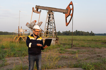 Engineer with a laptop against the background of oil rockers.