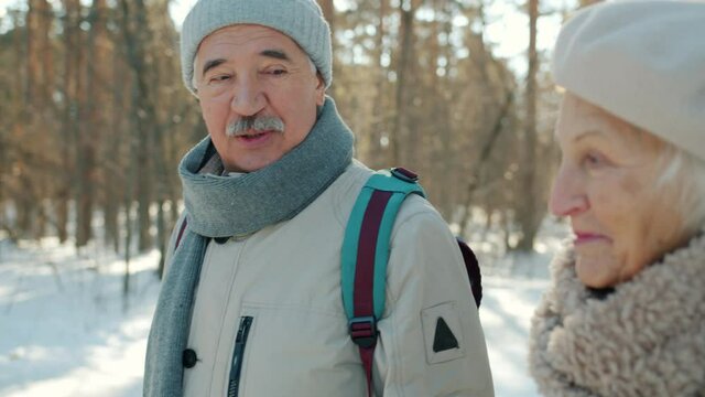 Slow motion of joyful senior people husband and wife walking in winter park smiling talking enjoying fresh air. Family outdoor activities and lifestyle concept.