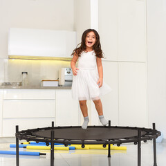 Happy little child jumping on trampoline in home.