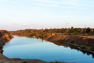 Obraz premium Wind turbine rises above small lake with blue water at the sunset. Renewable electricity generation theme.
