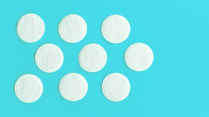 Nine white cotton cosmetic pads arranged on cyan blue board, closeup view from above