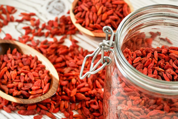 Dried goji aka. wolfberry seeds inside glass bottle, some more blurred in wooden bowls and spilled on white boards desk