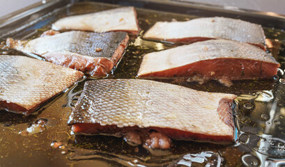 Raw salmon steaks with skin in cooking oil and some herbs on frying pan - to be baked, closeup...