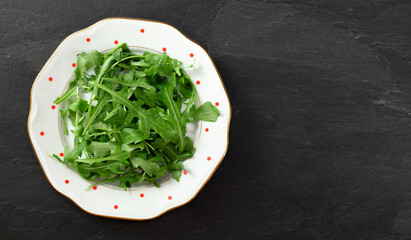 Fresh green arugula or garden rocket leaves on white plate with red dots, black table (space for text right side) under. Healthy greens and salads concept