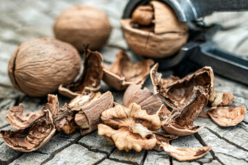 Whole and broken walnuts with walnut cracker on old rustic wooden background. Selective focus.