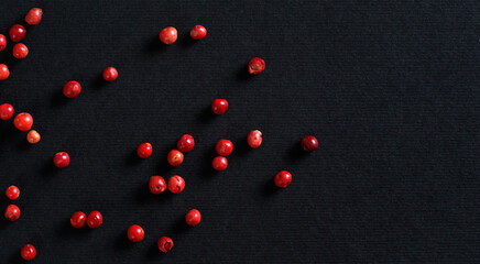 Whole pink / red peppercorns on black / gray paper, view from above, space for text right side