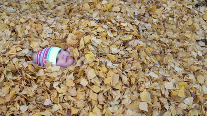 The girl completely buried herself in a pile of fallen leaves
